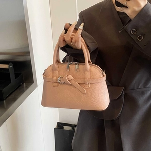 Detail of pink lychee leather handbag featuring decorative straps and dual zippers