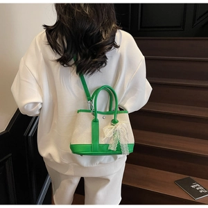Detail of canvas tote bag with green leather trim and decorative lace bow charm