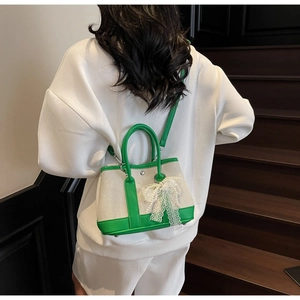 Detail of canvas bag with green leather trim and elegant white lace bow charm