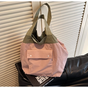 Detail of army green and pink tote bag with buttoned front pocket on a black leather seat