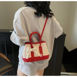 Detail of canvas bag with red leather trim, lace bow, and decorative pearl chains