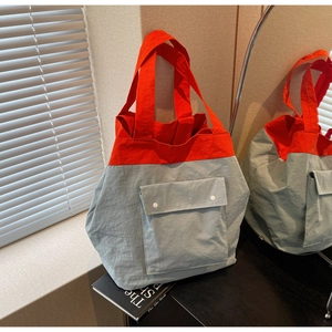 Detail of a large two-tone tote bag with a front flap pocket and orange shoulder straps