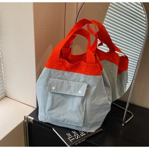 Detail of a large color-block tote bag in orange and blue nylon with snap-button front pocket