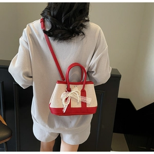 Detail view of canvas and red leather shoulder bag with lace bow and pearl charm