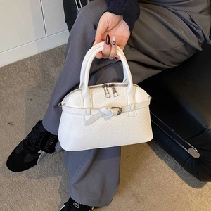 Detailed shot of white pebble grain leather handbag featuring dual zippers and tie-knot strap