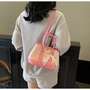 Detail of pink canvas handbag with lace bow and pearl charm on a model's shoulder