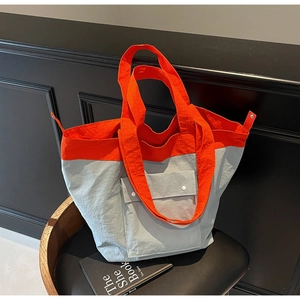 Detail of a large nylon tote bag with orange and blue contrast stitching and snap pocket