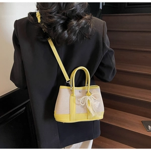 Mini canvas handbag with yellow leather trim and lace bow shown on a shoulder