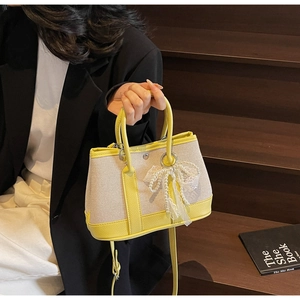 Detail of canvas bag with yellow leather trim and a pearl lace bow charm on wood steps