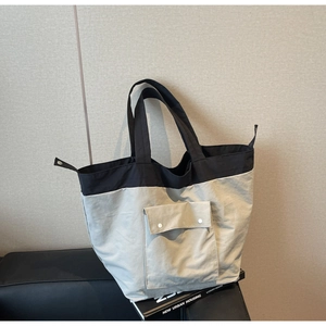 Detail of color-block tote bag showing front pocket with snap closure and nylon texture
