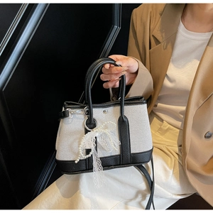 Detail of a minimalist black and white canvas bag with a lace pearl bow on a model