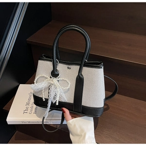 Detail of contrast stitch handbag with pearl bow charm on a minimalist canvas body
