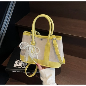 Detail of color-block tote bag with pearl lace bow charm on wooden stairs
