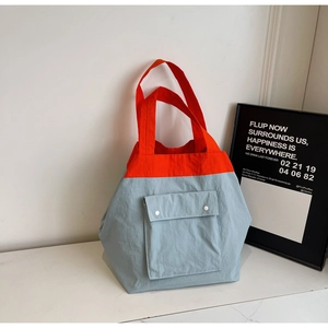 Detail view of the orange and blue contrast tote bag with functional front snap pockets