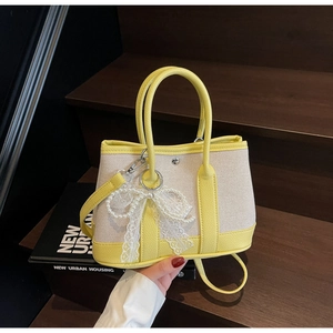 Canvas and yellow leather tote detail with pearl lace bow charm on dark wood steps