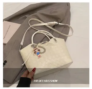 Detail of a beige woven tote bag with round handle, crossbody strap, and cute doll charm