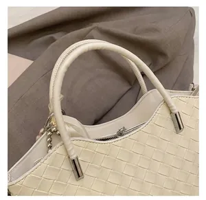 Detail of cream woven leather handbag featuring round handles and metallic zipper closure