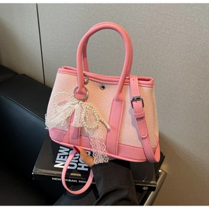 Detail of pink canvas tote with leather trim, pearl charm, and lace bow accessory