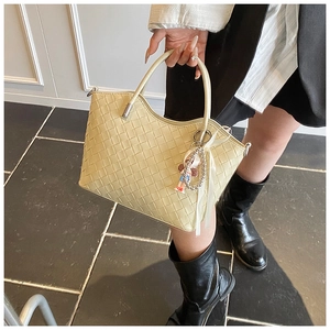 Detailed shot of beige quilted bucket bag with woven pattern and cute plush ribbon charm