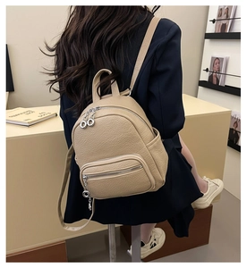 Detail of a beige pebbled leather mini backpack with silver zippers and multiple pockets