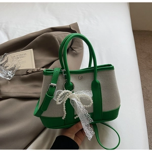 Detail of canvas bag with green leather trim, pearl bow and lace charm accessory