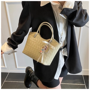 Detail of woven tote bag with ribbon bow and pearl charm worn with a stylish blazer