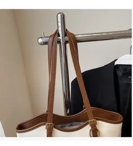 Detail of adjustable brown leather straps and gold buckles on a beige tote bag