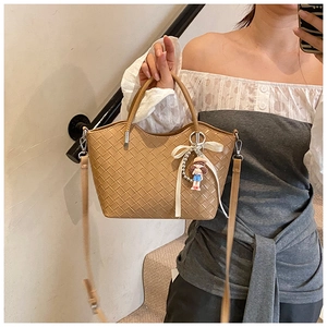 Detail of brown woven tote bag featuring a cute doll charm and velvet bow accessory
