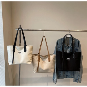 Detailed view of large canvas tote bags in white, beige, and black on a rack