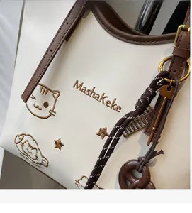 Detail of embroidered cat pattern and diverse decorative charms on the cream tote bag