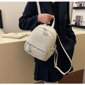 Close-up of cream pebble grain leather backpack featuring silver ring zippers and side pockets