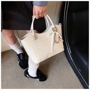 Close-up of cream woven bucket bag with side bow detail and charming doll pendant
