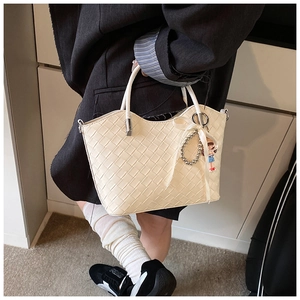 Detail of cream quilted handbag featuring weave pattern and cute charm on the handle