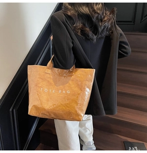 Borsa tote marrone con esterno in PVC e trama Tyvek mostrata sulla spalla del modello