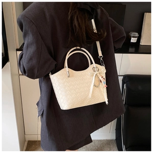 Detail of white woven PU leather bucket bag featuring a wavy rim and metallic handles