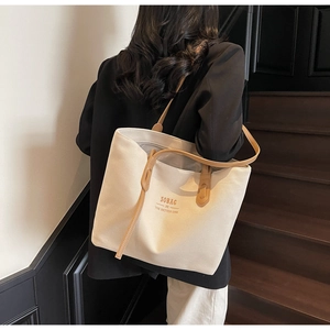 Rear view of a model carrying a beige canvas tote bag with brown leather straps and text