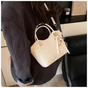 Detail of cream woven handbag featuring heart-shaped rim and elegant pearl bow charm