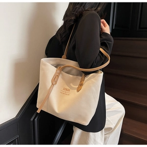 Detail view of large canvas tote bag with dual brown leather handles and printed logo