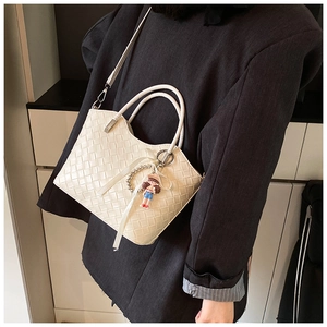 Detail of white woven bucket bag with doll charm on grey blazer shoulder