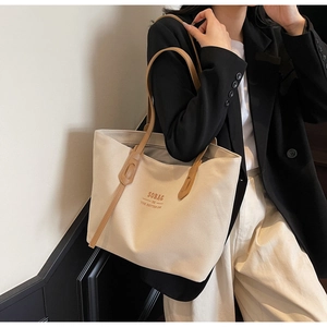 Detailed view of beige canvas tote bag with brown leather handles and slogan on a model