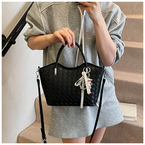 Detail of black woven tote bag with PU leather texture, luxury ribbon and plush charm