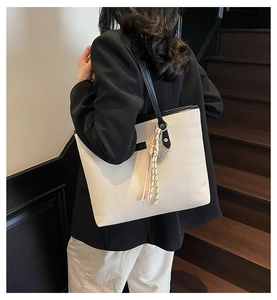 Detail of cream tote bag with embossed texture, black straps and decorative tassel charm