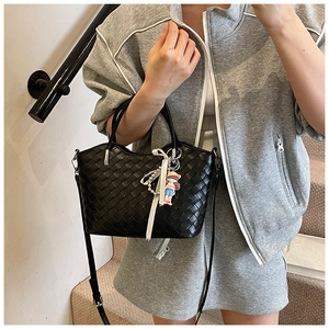 Detail of black woven shoulder bag with white bow and cartoon charm in lifestyle setting
