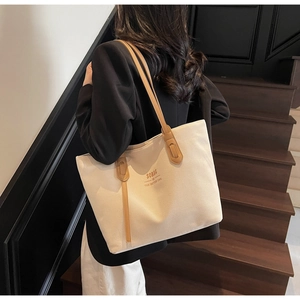 Lifestyle shot of an off-white canvas tote bag with brown leather handles on stairs