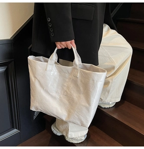 Dettaglio di una grande borsa tote bianca con scritta TOTE BAG su sfondo di scale scure