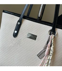 Detail of beige textured fabric tote with black leather handle and creative charm accessories
