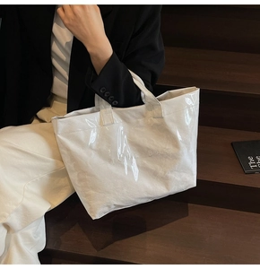 Dettaglio della borsa tote bianca lucida plissettata con testo nero su scala in legno
