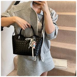 Detail of black woven leather bucket bag featuring a pearl charm and cartoon doll accessory