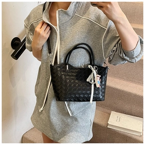 Detail of black woven handbag with pearl charm and white ribbon on a chic strap