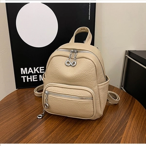 Detail of a beige pebbled leather mini backpack with silver ring zippers on a wooden table